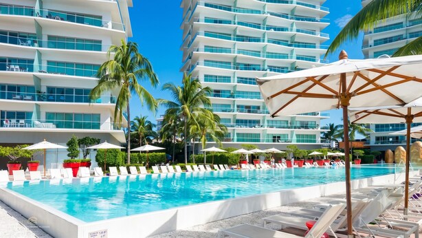 A swimming pool with lounge chairs and umbrellas, surrounded by palm trees and modern buildings. - Icon Vallarta · Style, Comfort and Pool (Puerto Vallarta)