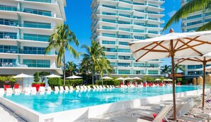A swimming pool with lounge chairs and umbrellas, surrounded by palm trees and modern buildings. - Icon Vallarta · Style, Comfort and Pool (Puerto Vallarta)