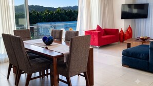 A modern living room with a dining area, a red sofa, and a TV mounted on the wall. - Icon Vallarta · Style, Comfort and Pool (Puerto Vallarta)