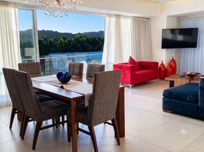 A modern living room with a dining area, a red sofa, and a TV mounted on the wall. - Icon Vallarta · Style, Comfort and Pool (Puerto Vallarta)