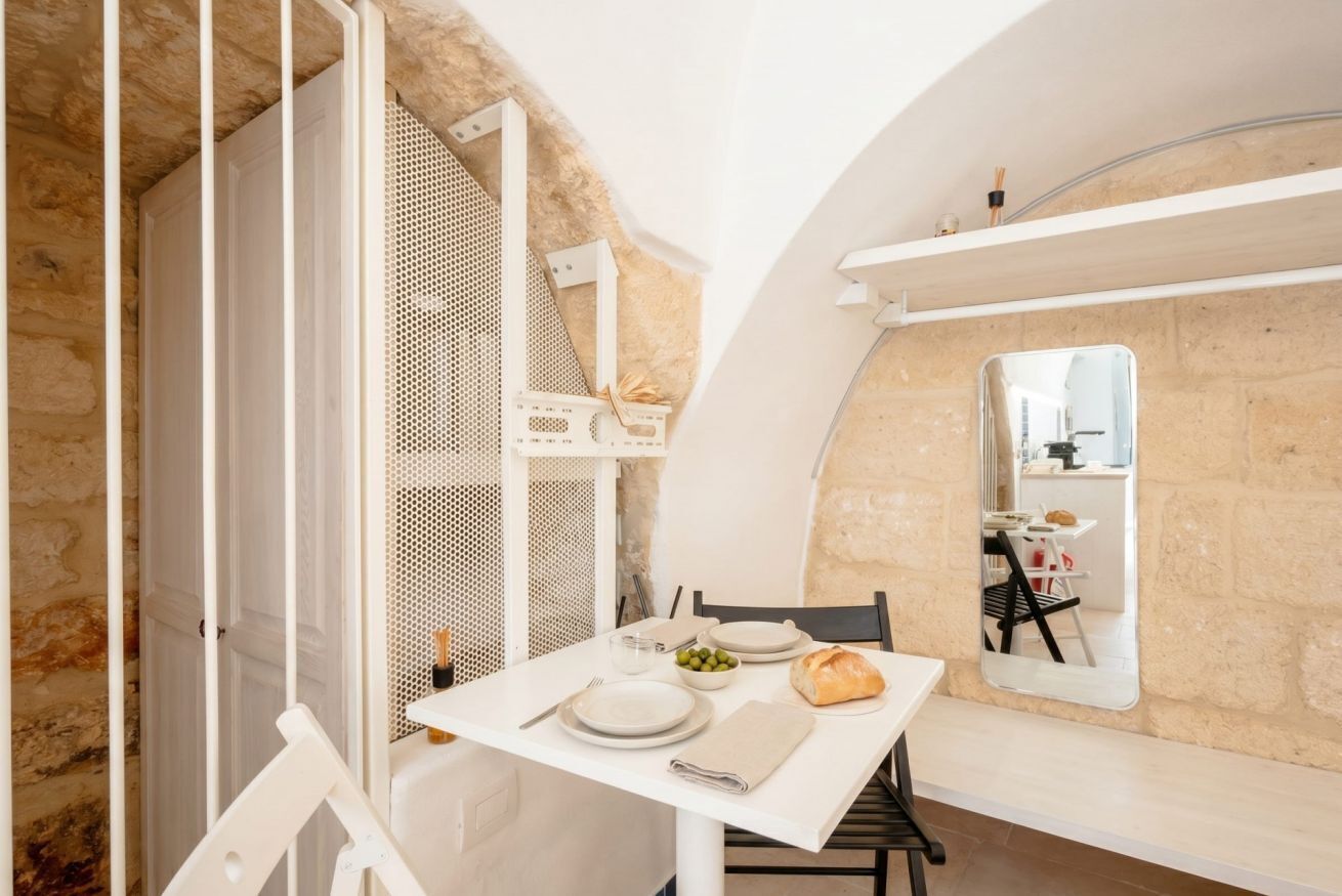 A dining area with a table set for two, a mirror, and a stone wall.