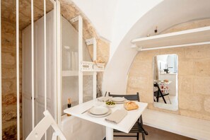 Un coin repas avec une table dressée pour deux personnes, un miroir et un mur en pierre.