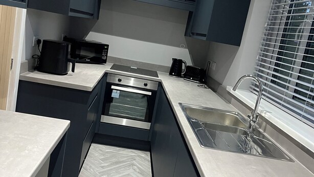 A modern kitchen with dark cabinetry, a built-in oven, a microwave, and a stainless steel sink. - Fabulous 3-bedroom house in charming Bircotes for your getaway (Bircotes)