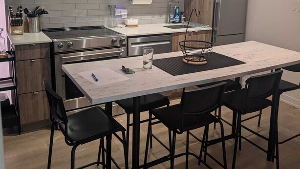 Uma cozinha moderna com eletrodomésticos de aço inoxidável, uma mesa de jantar com cadeiras e uma luminária pendente.