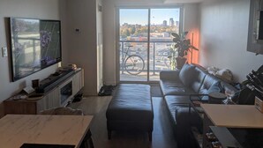 Uma sala de estar moderna com uma TV grande, um sofá, uma mesa de jantar e uma varanda com vista para a cidade.