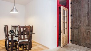 A dining area with a table set for four, a hanging pendant light, and a wooden door with a red frame. - Grand Historic Alfama Apartment, 4BR, 2WC (Lisboa)