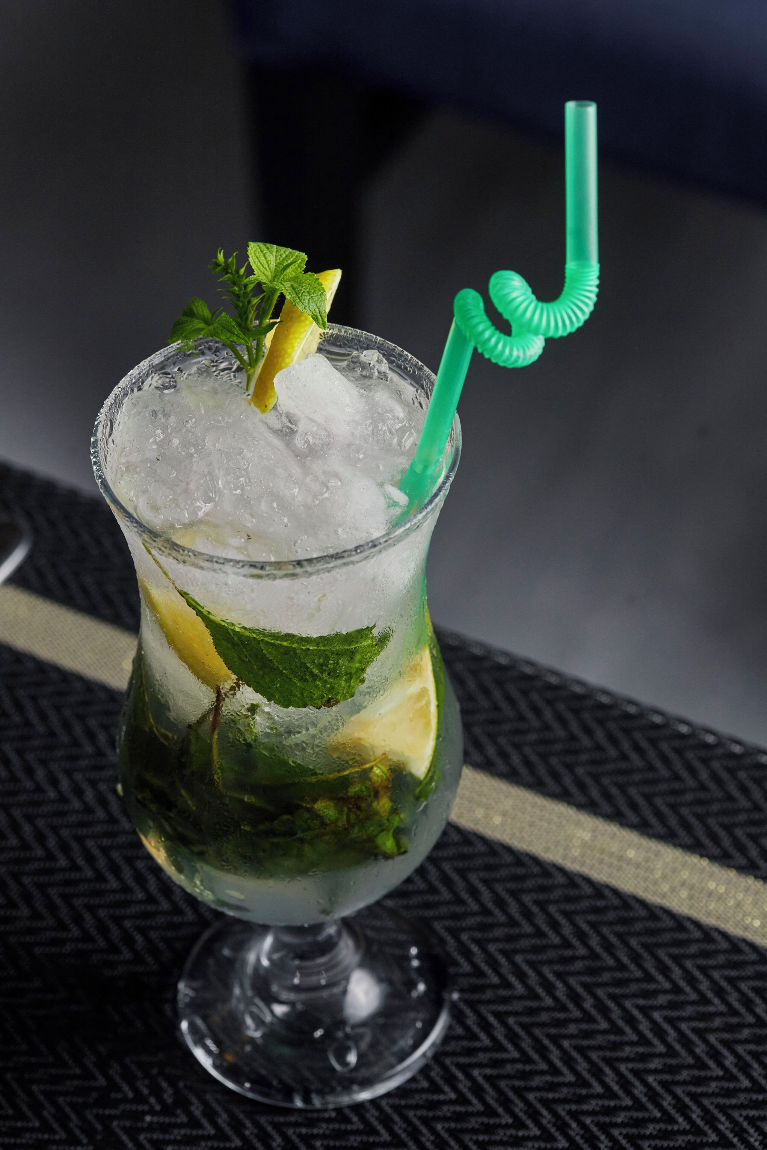 A glass with ice, mint leaves, and a lime slice, with a green straw.