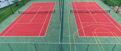 A tennis court with a net, surrounded by a fence, and adjacent buildings.
