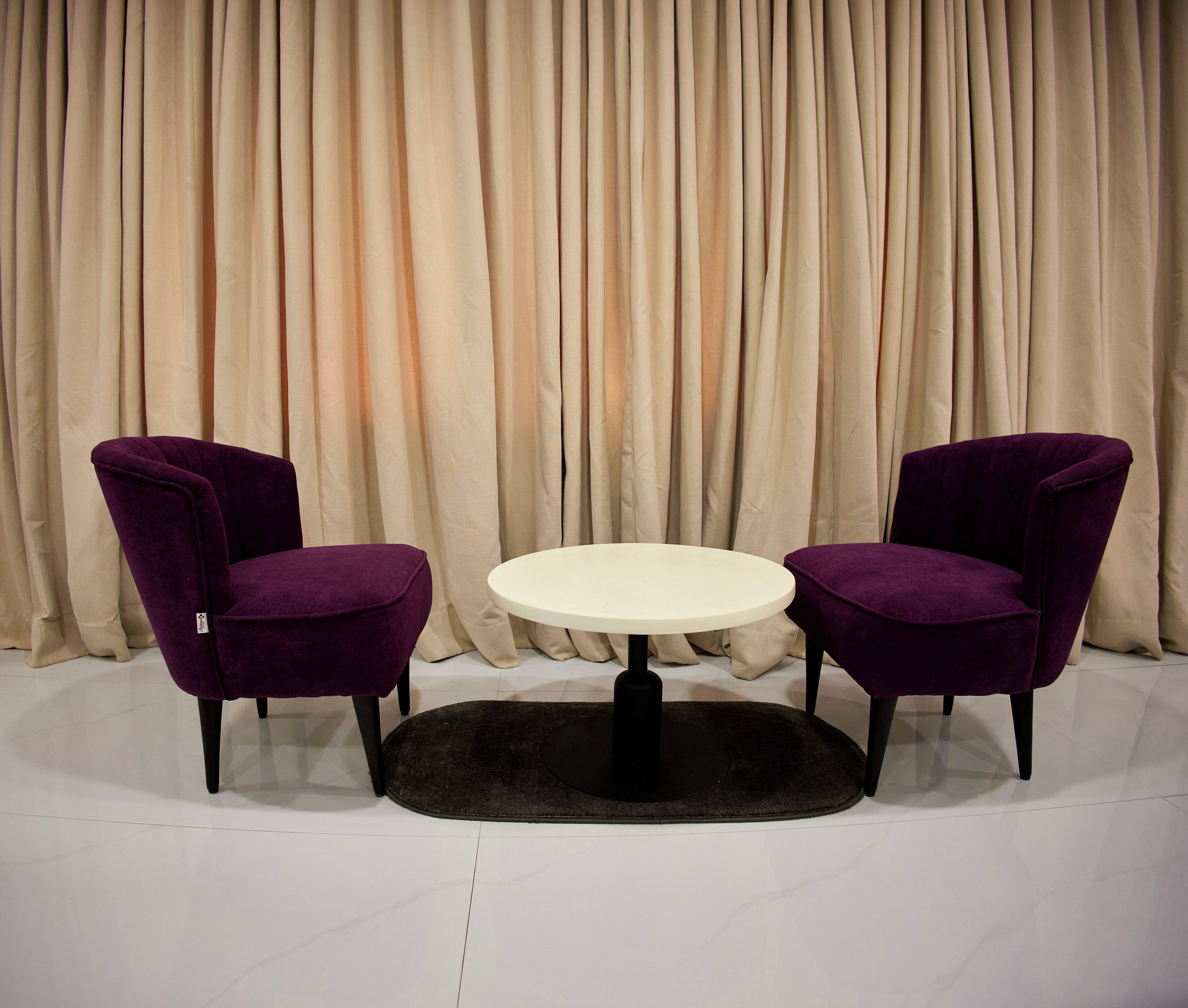 Una habitación con dos sillas moradas, una mesa redonda y un tapete negro.
