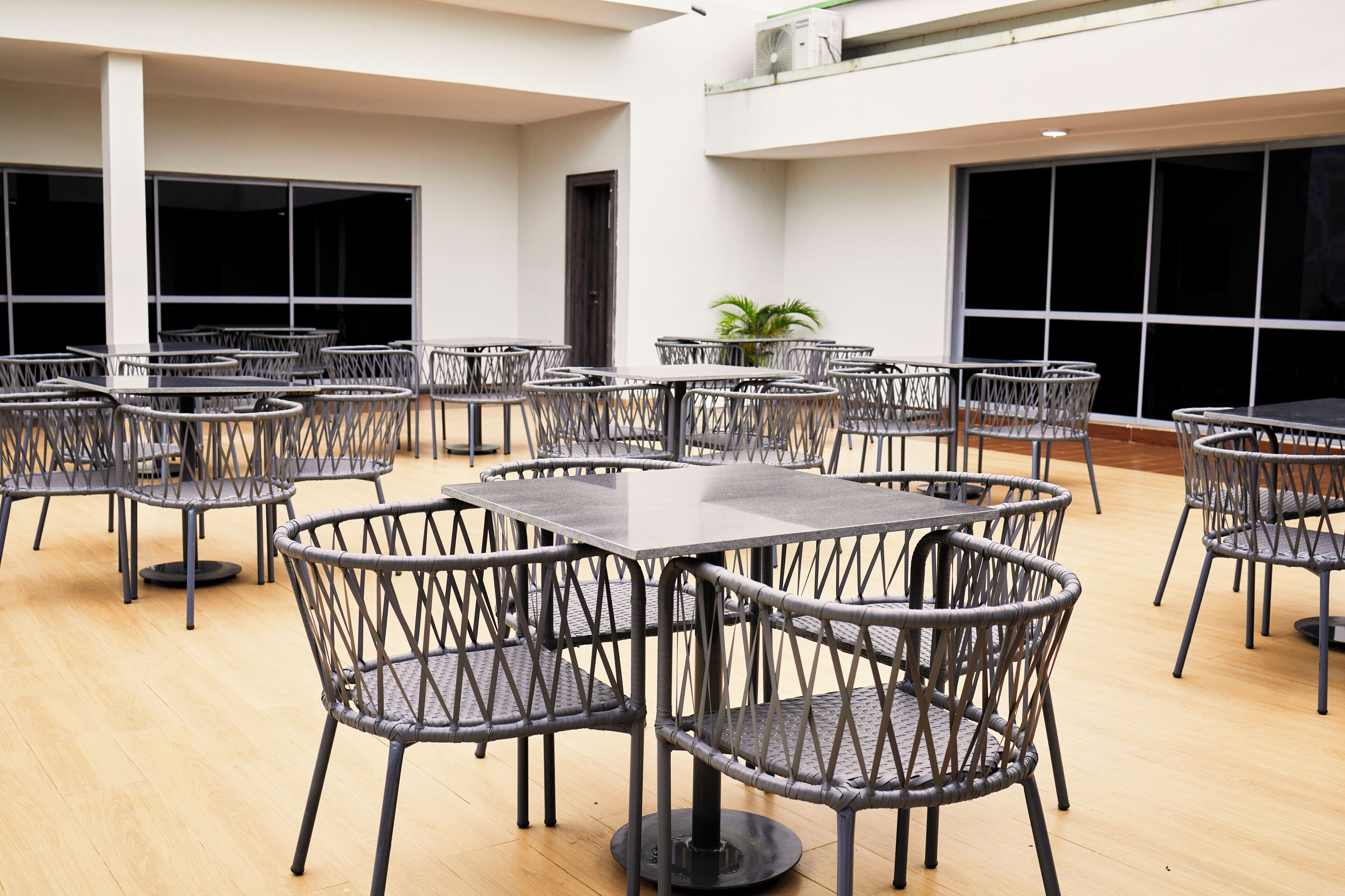 A spacious indoor area with multiple tables and chairs, large windows, and a potted plant.