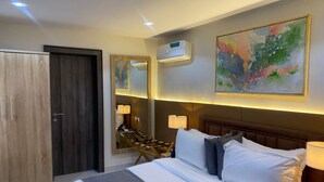 Habitación de hotel con cama, armario de madera, espejo, un cuadro y unidad de aire acondicionado.