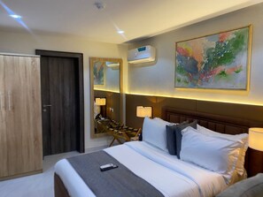 Habitación de hotel con cama, armario de madera, espejo, un cuadro y unidad de aire acondicionado.