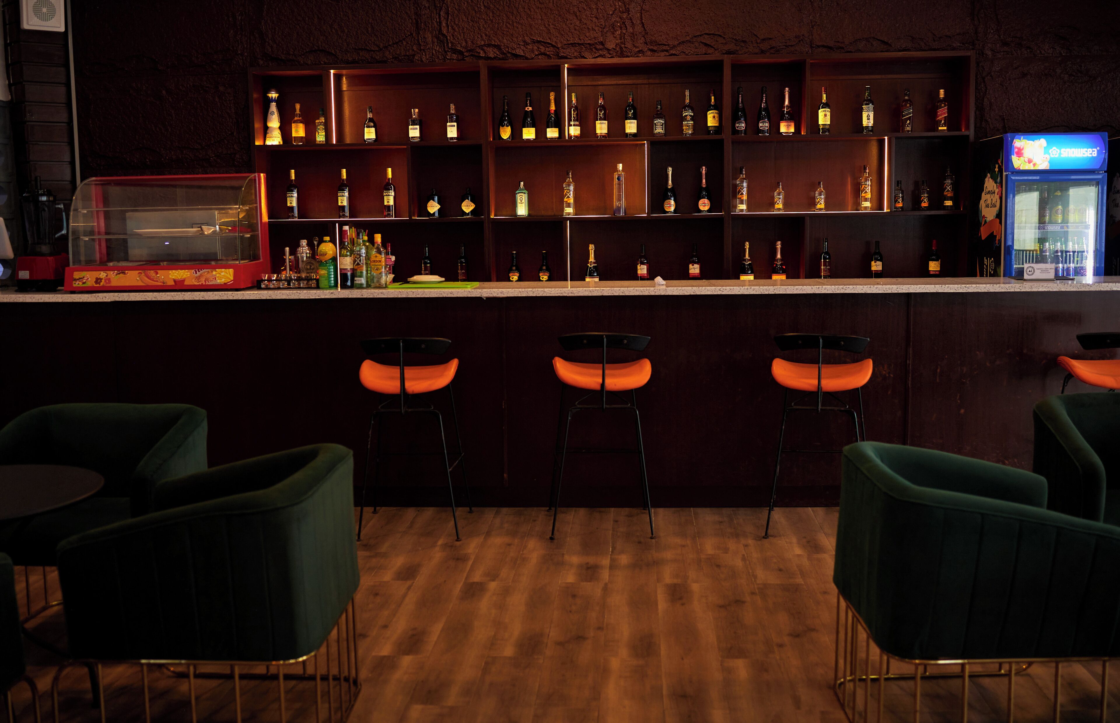 Eine Bar mit Holzböden, voll mit Flaschen, einer Kasse und orangefarbenen Barhocker.