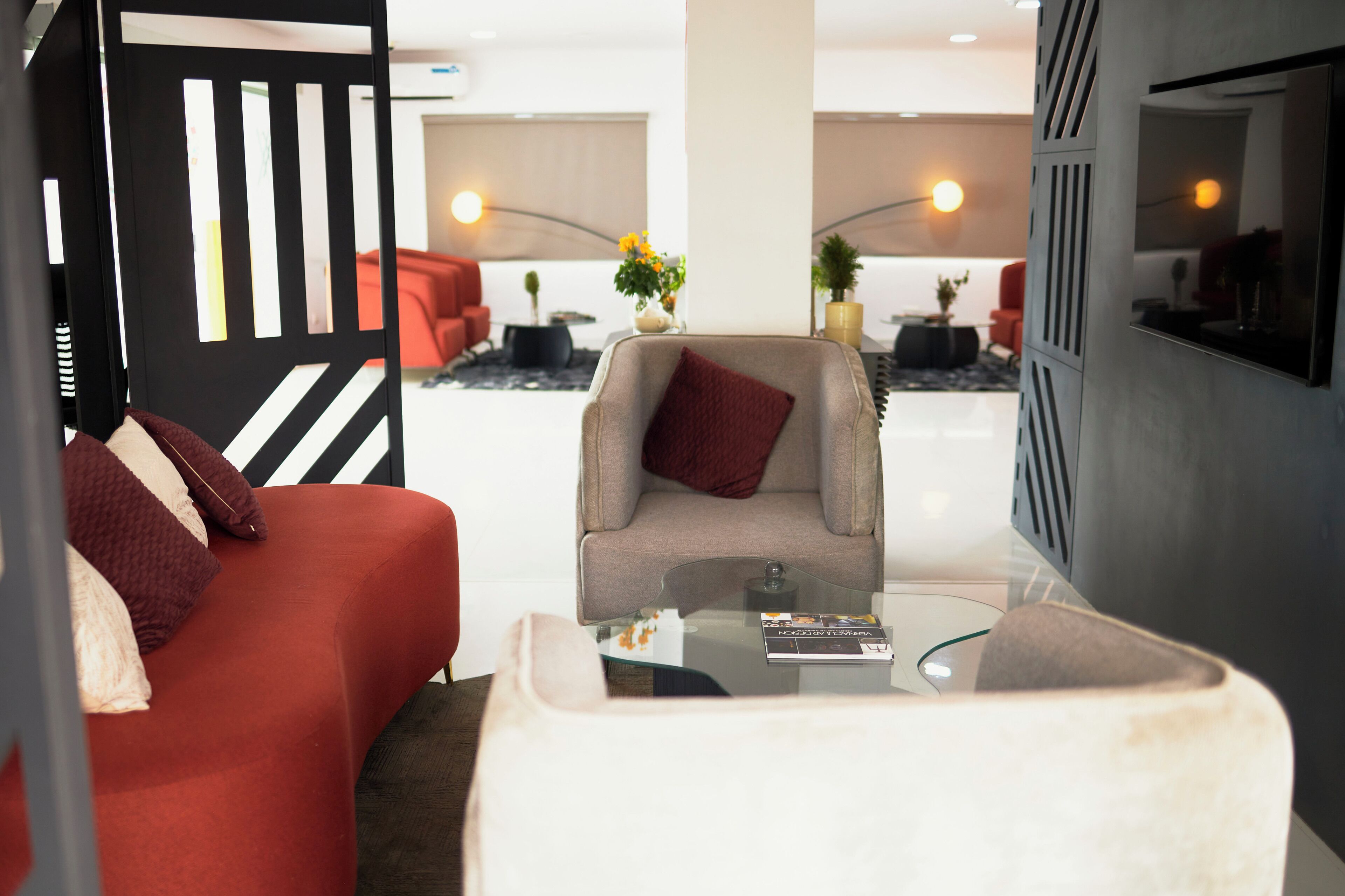 Un hall d’hôtel moderne avec un canapé rouge, un fauteuil gris, une table basse en verre et un vase décoratif rempli de fleurs.