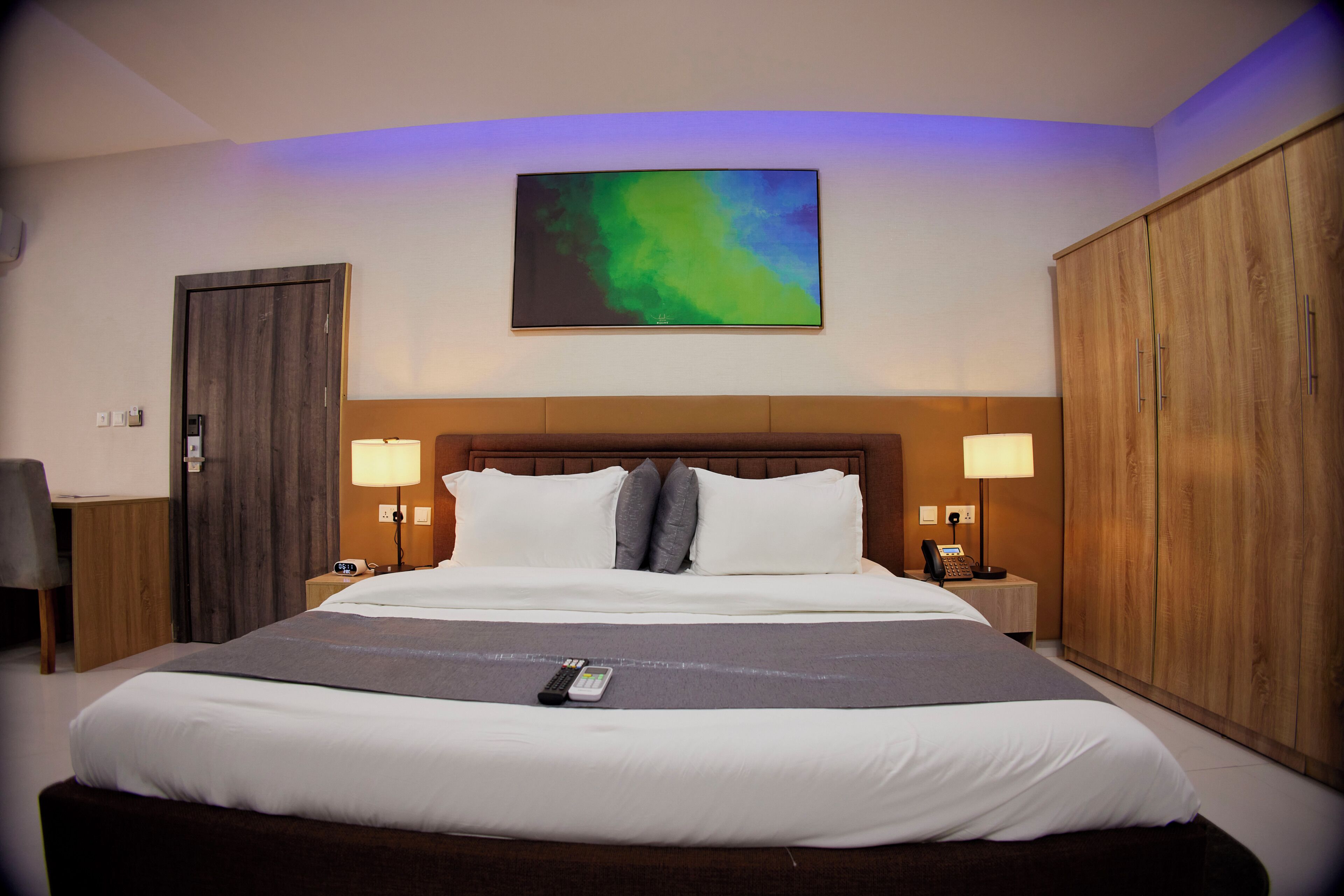 A hotel room with a large bed, two bedside tables with lamps, a wooden wardrobe, and a painting on the wall.
