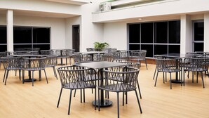 Un espacio interior amplio con varias mesas y sillas, ventanas grandes y unidades de aire acondicionado.