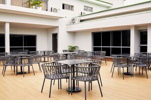 Un espacio interior amplio con varias mesas y sillas, ventanas grandes y unidades de aire acondicionado.