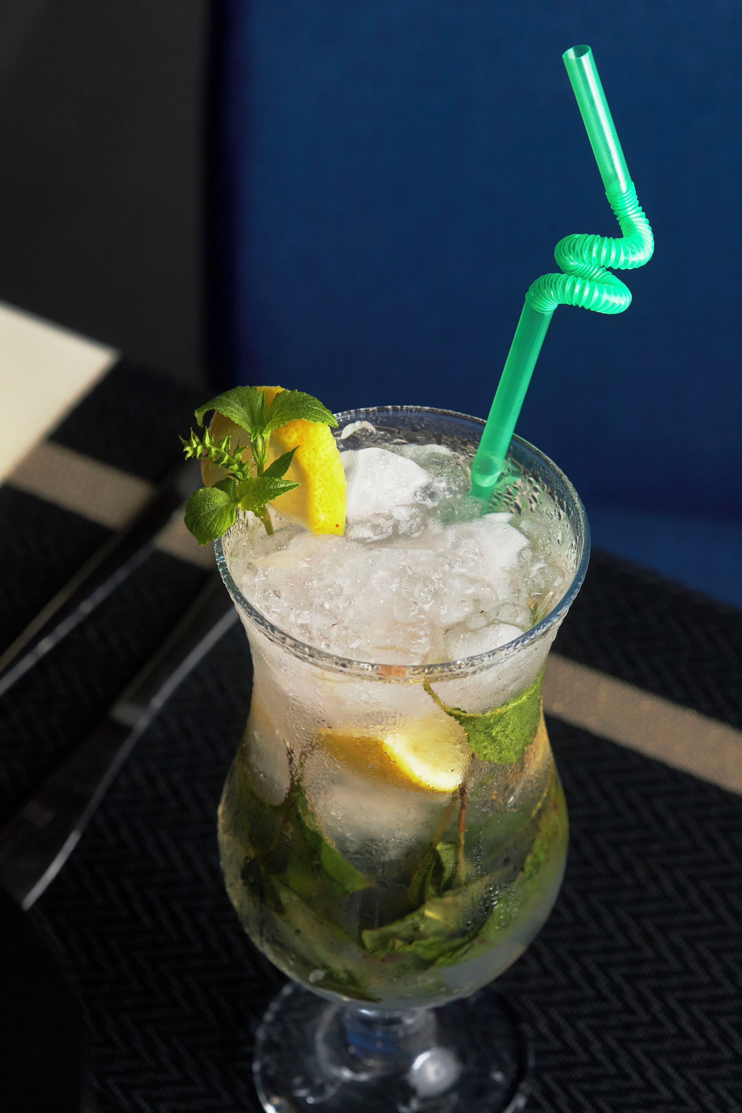 Un vaso con hielo, limón, menta y una pajita verde.