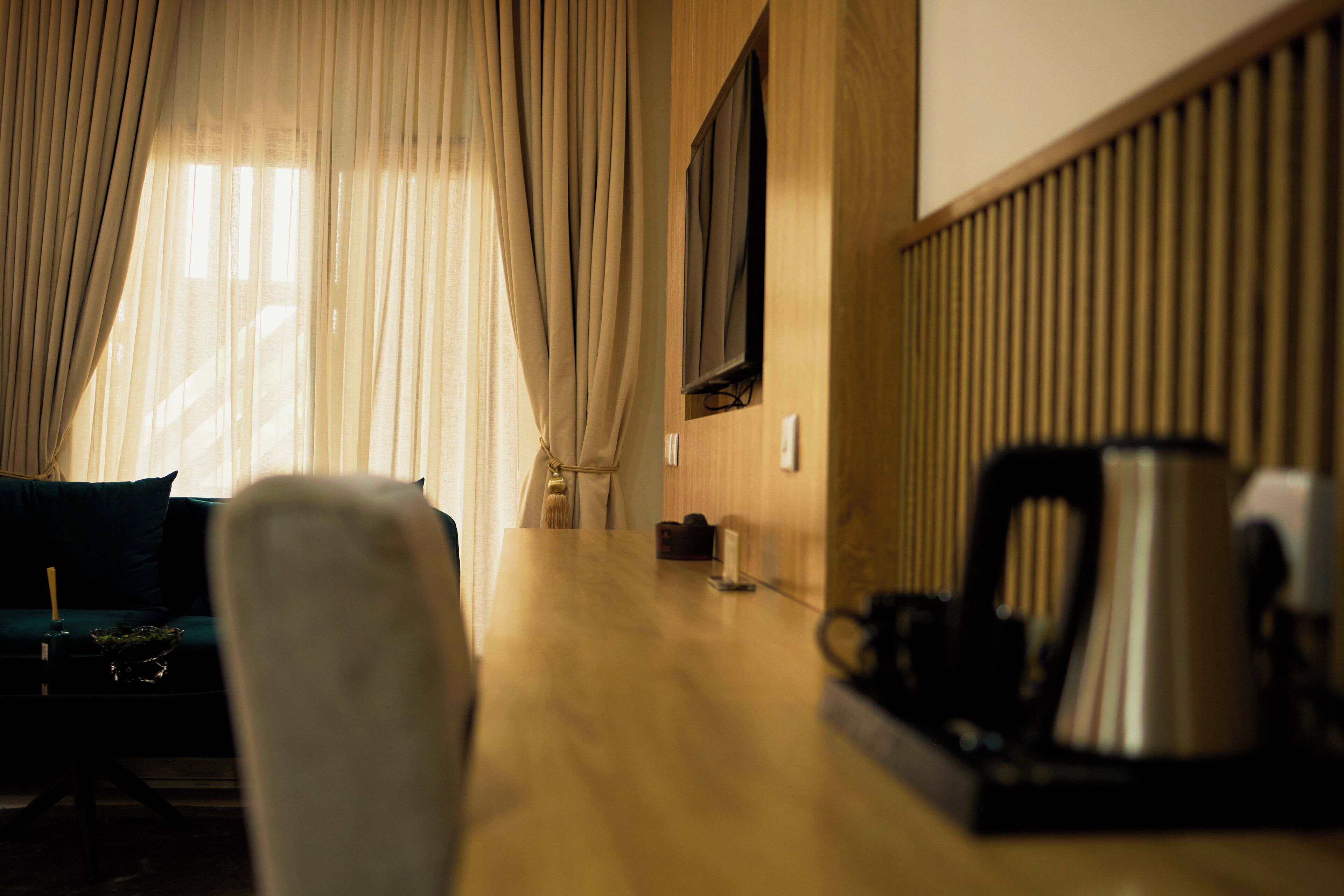 Een kamer met een houten tafel, een bank, een aan de muur bevestigde televisie en een raam met gordijnen.