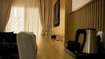 Een kamer met een houten tafel, een bank, een aan de muur bevestigde televisie en een raam met gordijnen.