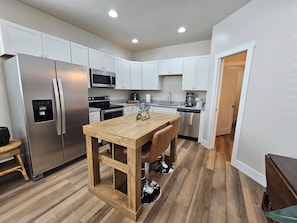 A modern kitchen with white cabinets, stainless steel appliances, a wooden island with bar stools, and a visible water dispenser. - Charming 1-bedroom apartment with AC in Fort Mill (Fort Mill)