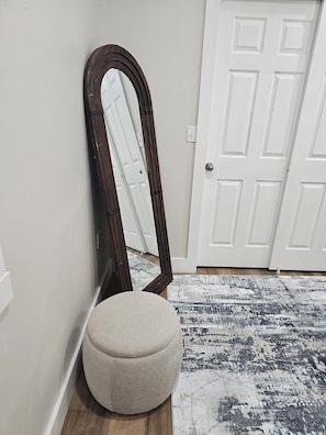 A room with a large mirror, a round ottoman, a patterned rug, and a white door. - Charming 1-bedroom apartment with AC in Fort Mill (Fort Mill)