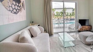 Un soggiorno con divano, tavolino in vetro, mobile TV e vista su una piscina e area salotto all'aperto.