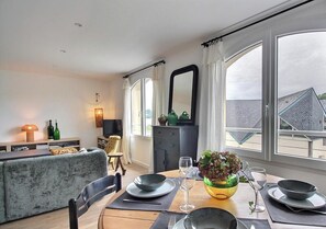 Ein Essbereich mit einem Tisch für zwei Personen, einer Couch, einem Fernseher und Blick ins Freie.