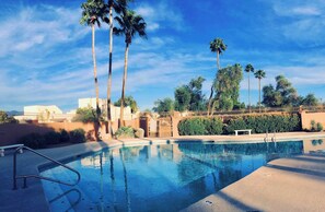 A swimming pool with a metal ladder, surrounded by palm trees and a fence, with buildings in the background. - 3-Bdrm / 2 Bath Townhome in Beautiful Tucson with AC and Parking (Tucson)