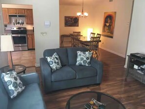 A living room with a sofa, a glass coffee table, and a dining area with chairs and a table. - 3-Bdrm / 2 Bath Townhome in Beautiful Tucson with AC and Parking (Tucson)