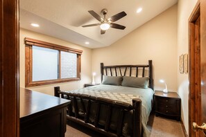 A bedroom with a sloped ceiling, a bed with a wooden headboard, a nightstand, a desk, and a window with blinds. - Park City townhome with 2 bedrooms, den, and 3 baths. (Park City)