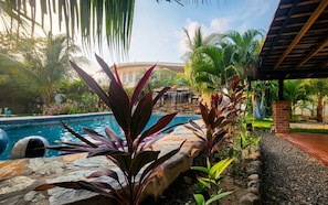 A pool with a waterfall, surrounded by tropical plants and a brick structure.