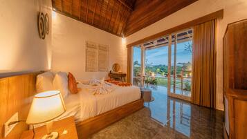 A bedroom with a bed, a bedside lamp, a wooden headboard, a window with curtains, and a view of the outdoors.