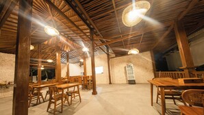 A spacious room with wooden tables and chairs, a stone wall, and a ceiling with wooden beams and hanging lights. - Lavanaa Nila-Luxury Resort (Penida Island)