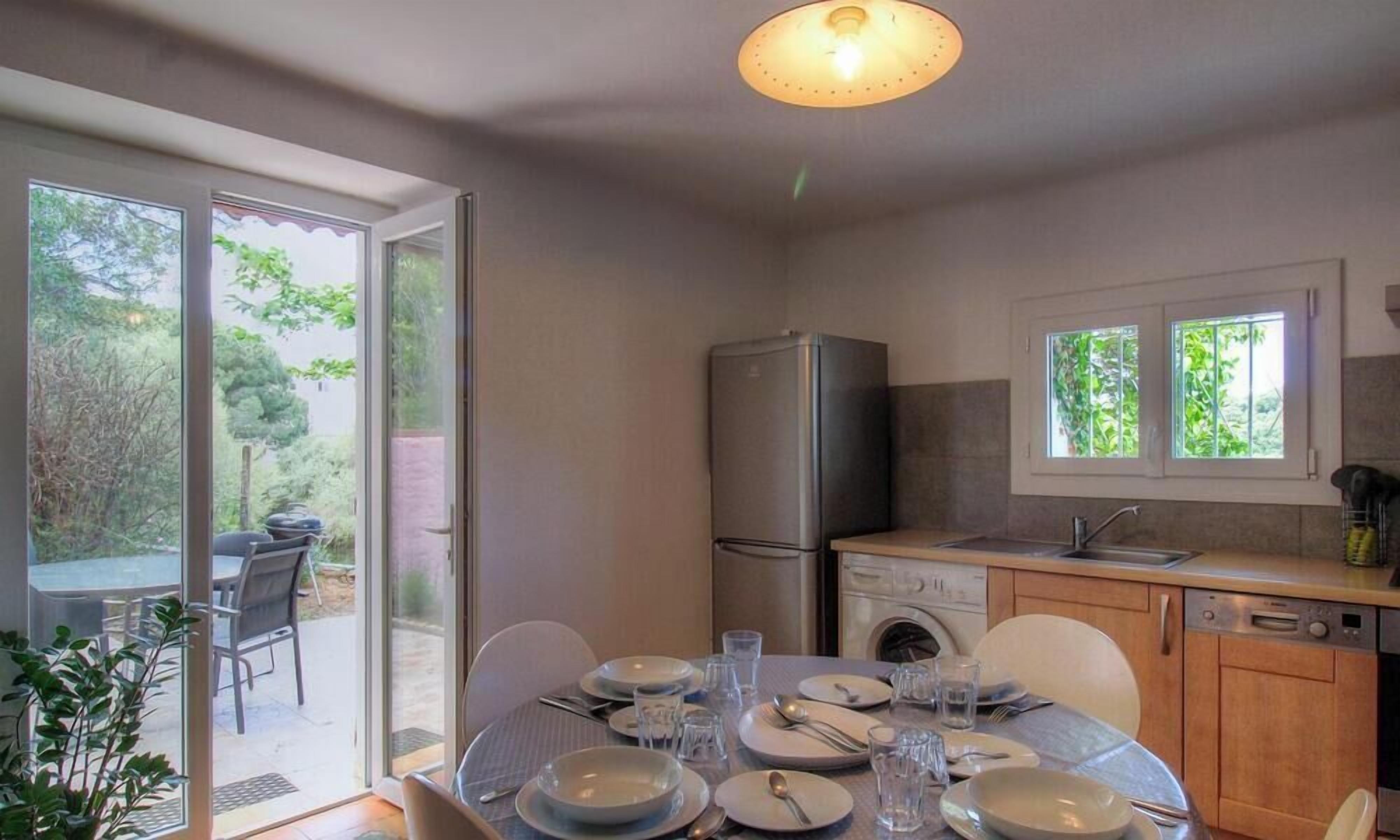 Ein Essbereich mit einem Tisch für vier Personen, einem Kühlschrank, einer Spüle und einem Fenster mit Blick auf einen Garten.