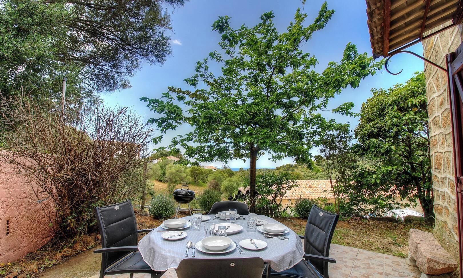 Un espace de restauration en plein air avec une table dressée pour quatre personnes, entourée de chaises, et offrant une vue sur la campagne.