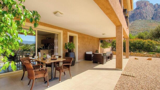 Un patio exterior con mobiliario de mimbre, una mesa de comedor y plantas en macetas.