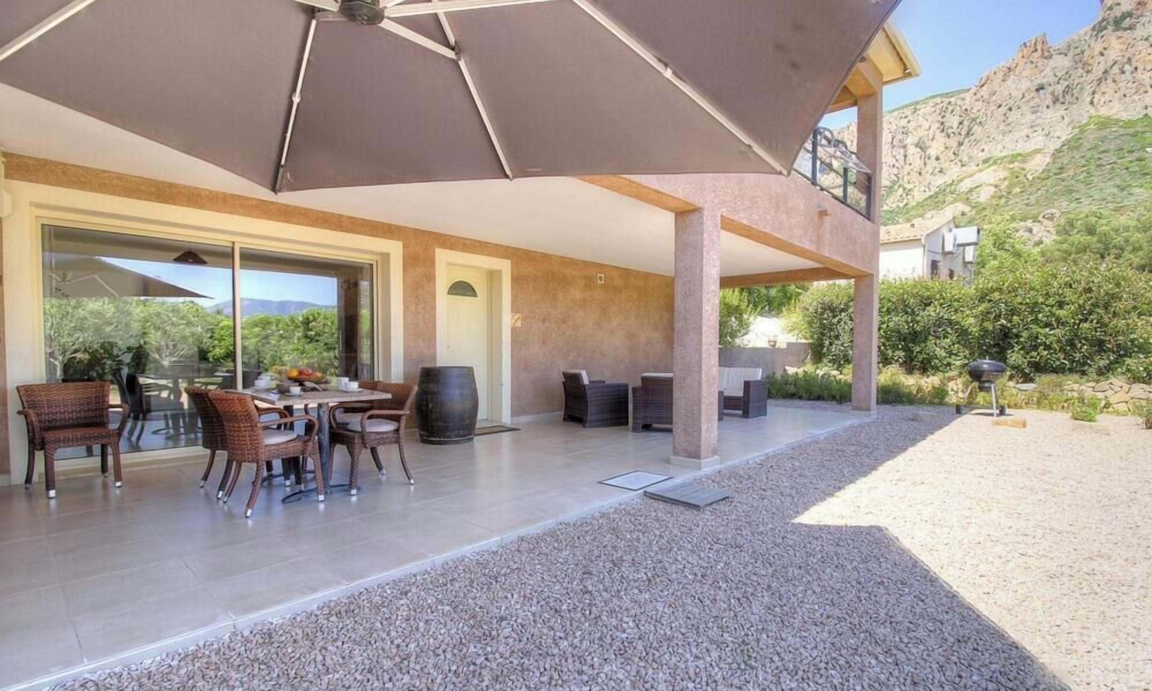 Une terrasse extérieure avec une table et des chaises, un grand parasol et une vue sur un paysage montagneux.