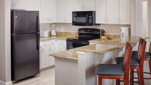 Une cuisine avec des meubles blancs, un réfrigérateur noir, un four à micro-ondes, une cuisinière et des plans de travail en granit.