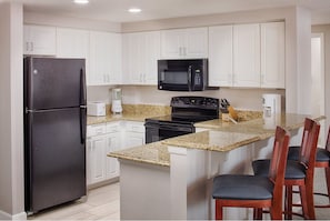 A kitchen with white cabinets, a black refrigerator, a microwave, a stove, and granite countertops. - Cozy 2 Bedroom Suite in Daytona Beach! rts (Daytona Beach)