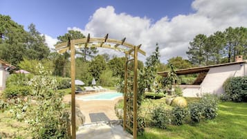 Ein Garten mit Pool, einer Holzpergola und einem weißen Gebäude.