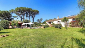 Ein gepflegter Garten mit Schwimmbecken, einer Terrasse mit Sonnenschirmen und einem Haus mit Ziegeldach.