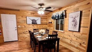 A dining room with a wooden table set for four, surrounded by chairs, with a ceiling fan above and a window with a view of trees. - B & T's Garden Getaway-Located in Historic Parowan near Brianhead Ski Resort (Parowan)