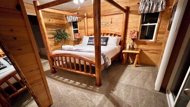 A wooden four-poster bed with a headboard, a bedside table, a lamp, and a window with curtains. - B & T's Garden Getaway-Located in Historic Parowan near Brianhead Ski Resort (Parowan)