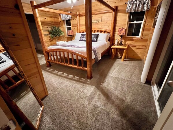 Una cama con dosel de madera, un cabecero, una mesita de noche, una lámpara y una ventana con cortinas.