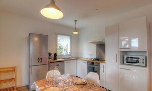 Cocina compacta con refrigerador, horno, microondas y una mesa de comedor para dos personas.