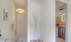 Un pasillo con un perchero, una lámpara colgante y una cocina visible a través de una puerta abierta.