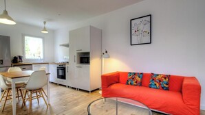 A modern kitchen with white cabinets, a dining table with chairs, a red sofa with colorful cushions, and a glass coffee table. - Campo Sotano - VENACO (VENACO)