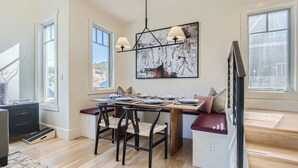 Een eetgedeelte met een houten tafel voor vier personen, een bank met kussens en een moderne kroonluchter.