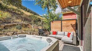 Ein Whirlpool mit einer Holzterrasse, ein Rattansofa mit roten Kissen und ein Holzzaun.